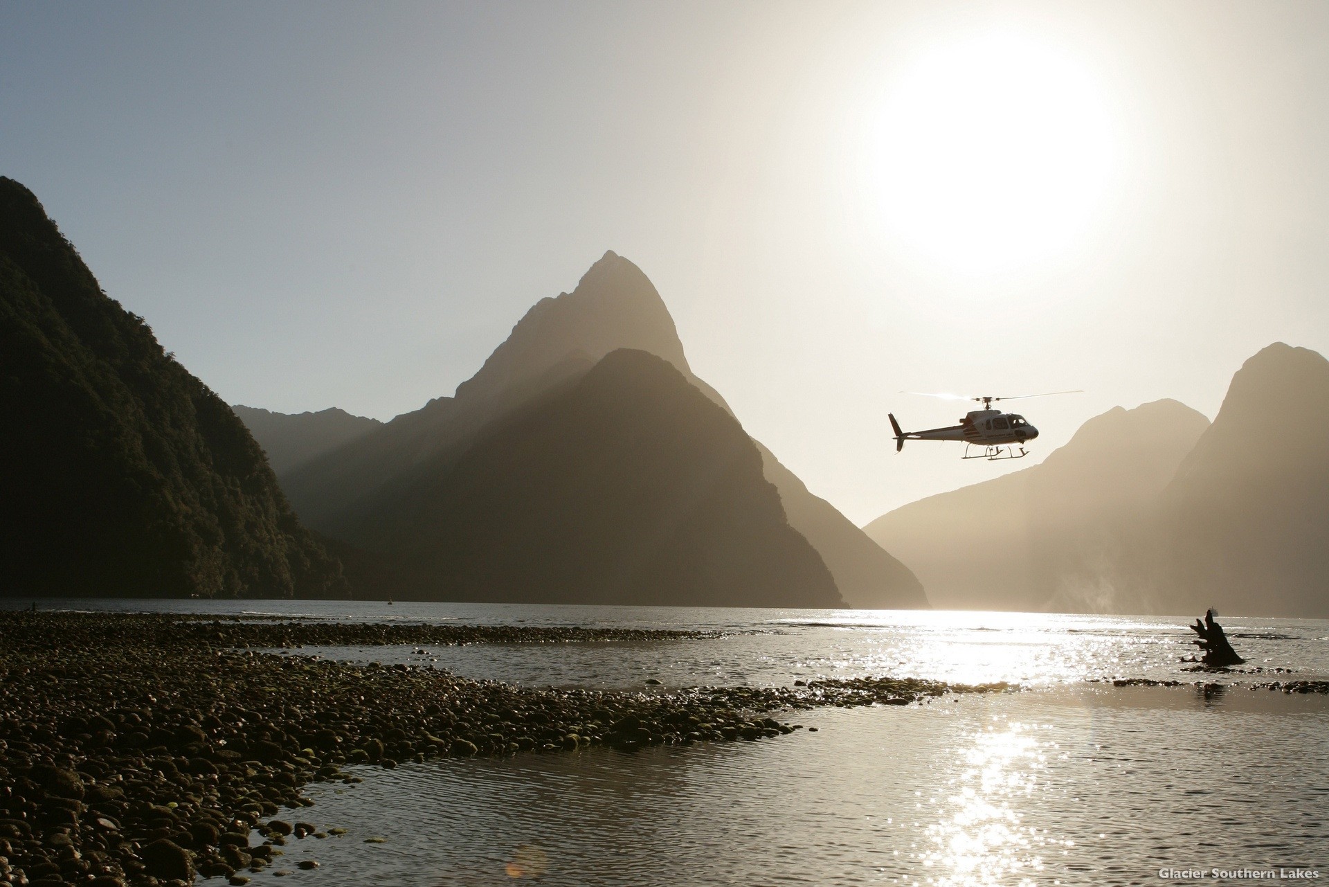 Helikopter fliegt über Wasser mit Bergen im Hintergrund