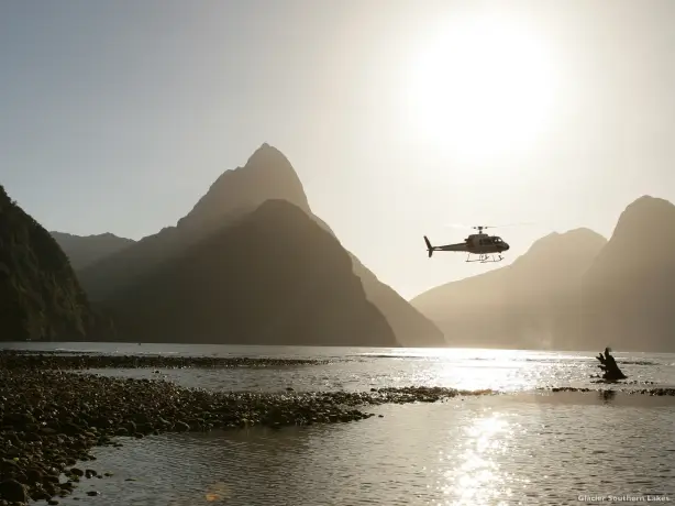 Helikopter fliegt über Wasser mit Bergen im Hintergrund