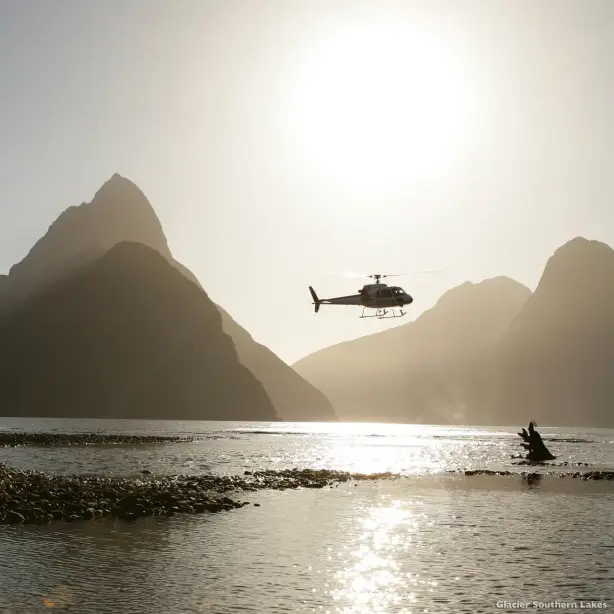 Helikopter fliegt über Wasser mit Bergen im Hintergrund