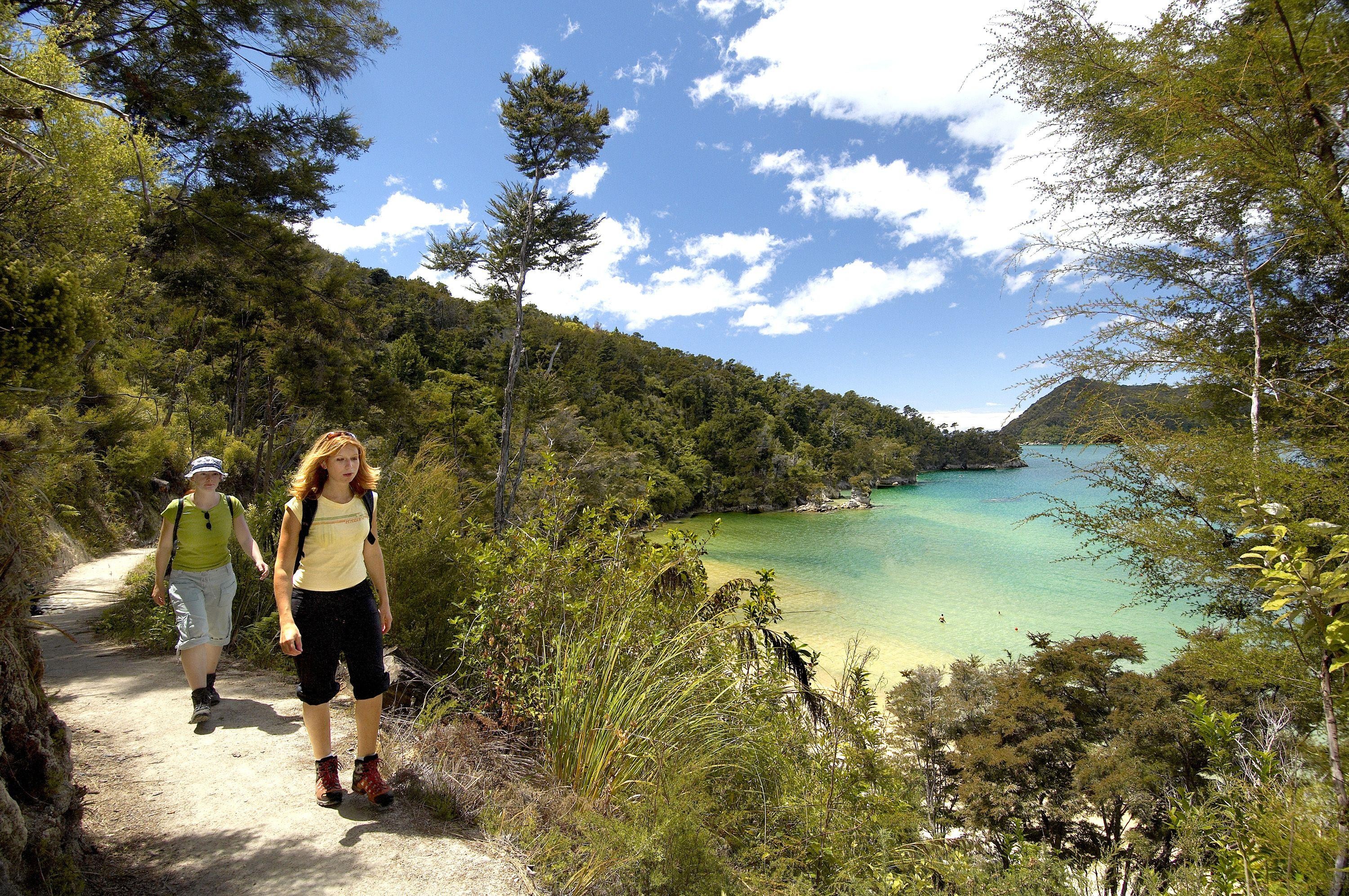 Two people walking a coastal path with a bay and forrest beside them