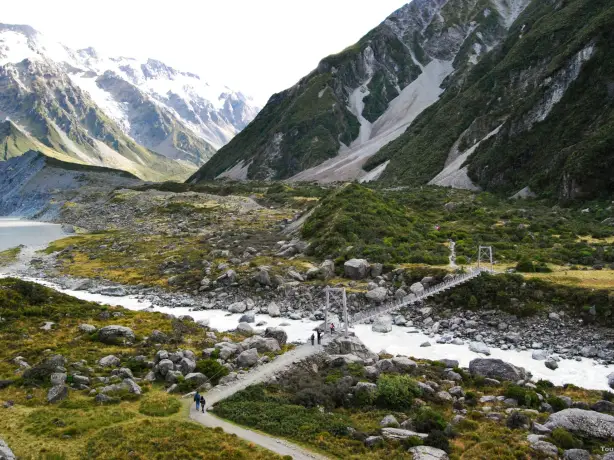 Brücke geht über Gebirgsfluss, schneebedeckte Berge im Hintergrund