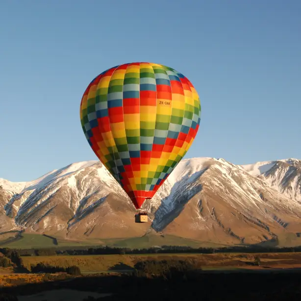 A multicolored hot air balloon with snow-capped mountains behind