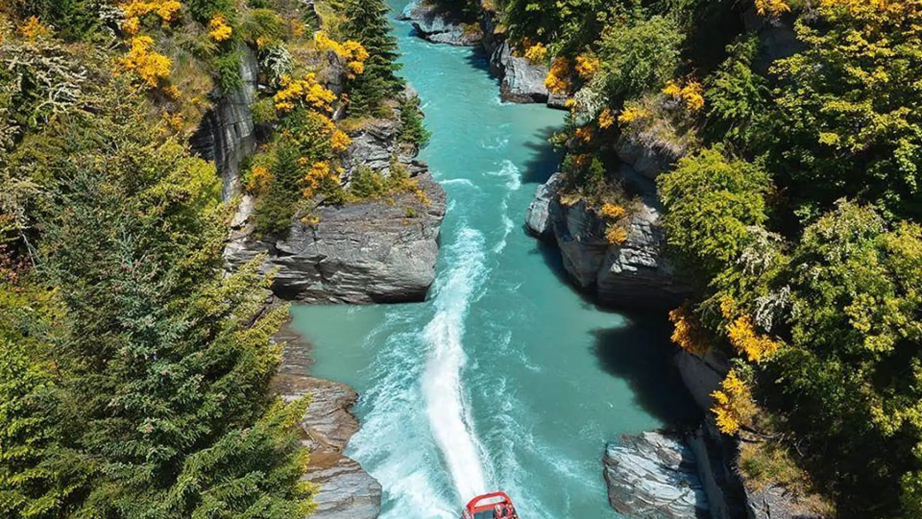 Ein Boot fährt auf einem Fluss zwischen Felsen und Wald in Neuseeland