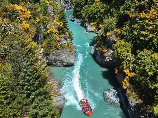 A boat moving along a river between rocky and forest terrain in New Zealand