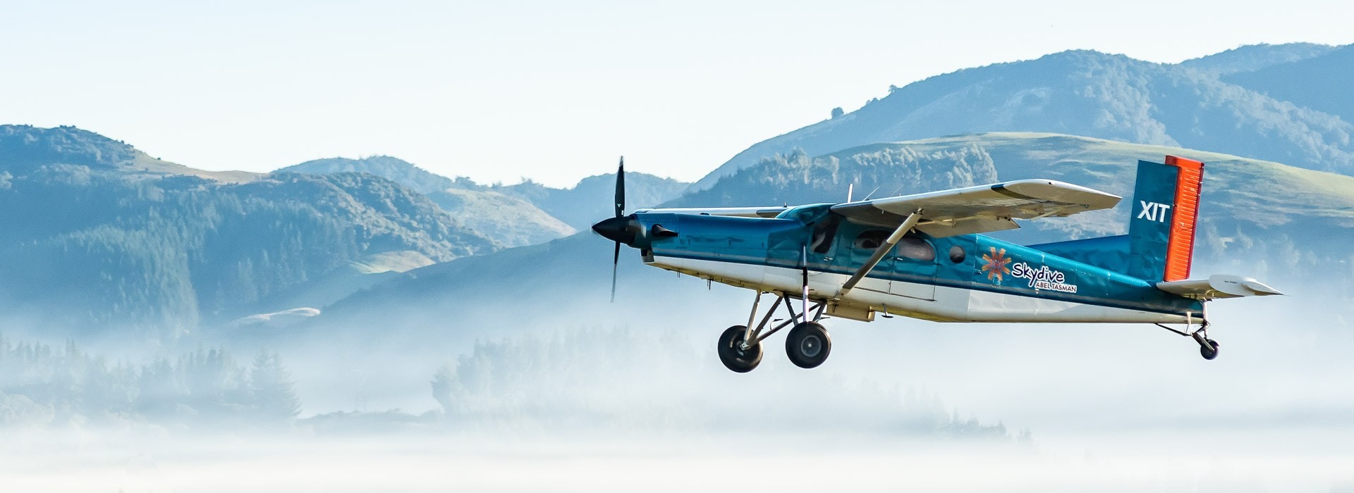 Kleinflugzeug fliegt vor nebeliger Hügellandschaft