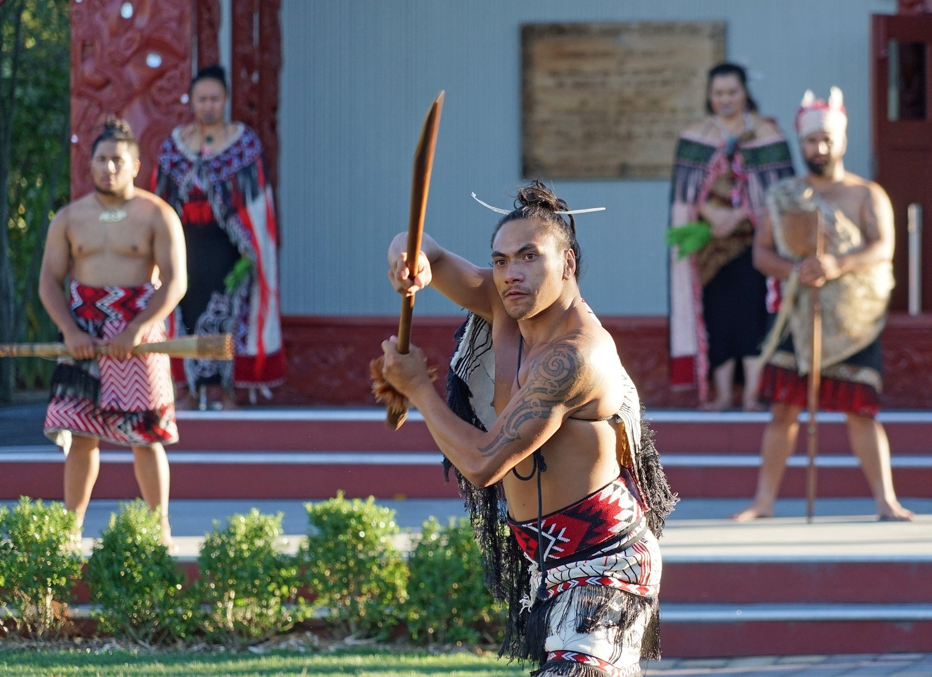 Eine Gruppe Māori-Männer in traditioneller Kleidung hält hölzerne Waffen (Taiaha)