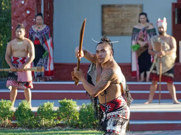 Eine Gruppe Māori-Männer in traditioneller Kleidung hält hölzerne Waffen (Taiaha)
