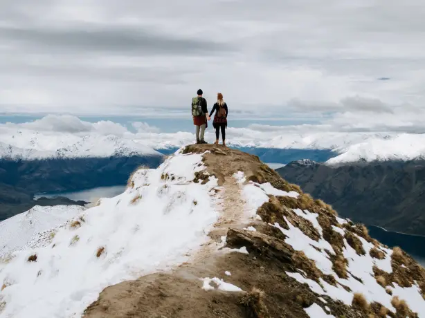 Paar steht auf einem Berggipfel und blickt über Berggipfel und Fjorde