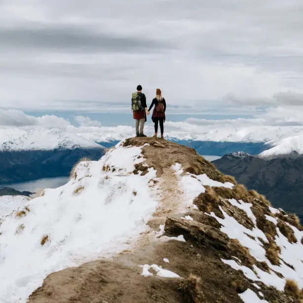 Paar steht auf einem Berggipfel und blickt über Berggipfel und Fjorde