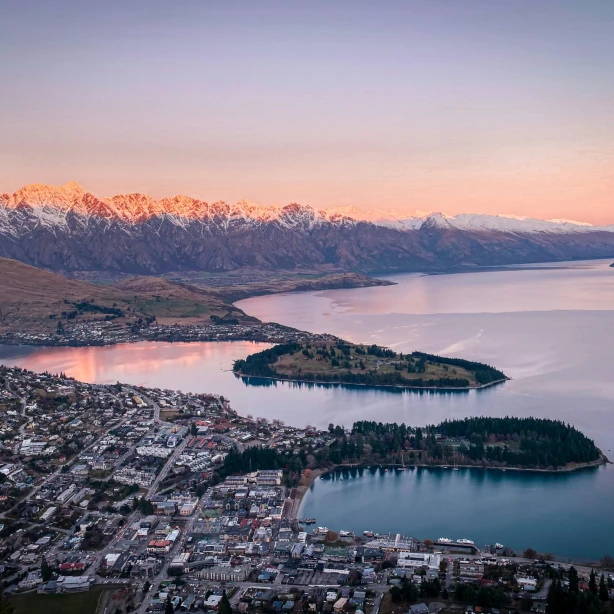 Uitzicht van bovenaf over Queenstown en op het omringende landschap van de besneeuwde bergen en het meer met de kleurrijke lucht - Nieuw-Zeeland