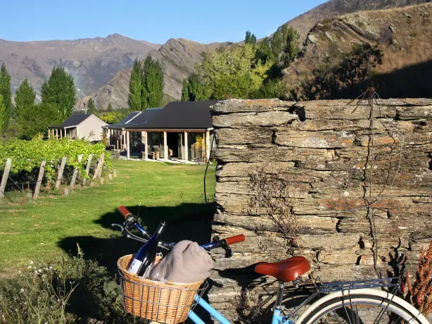 Fahrrad lehnt an Felsmauer, Weingut und Berge im Hintergrund