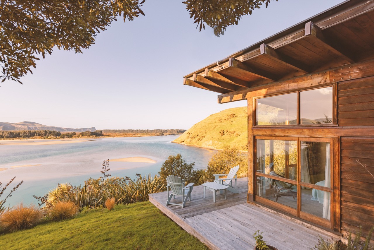 Stilvolles Holzhaus mit Terrasse und zwei Stühlen mit Blick über eine Bucht in Neuseeland