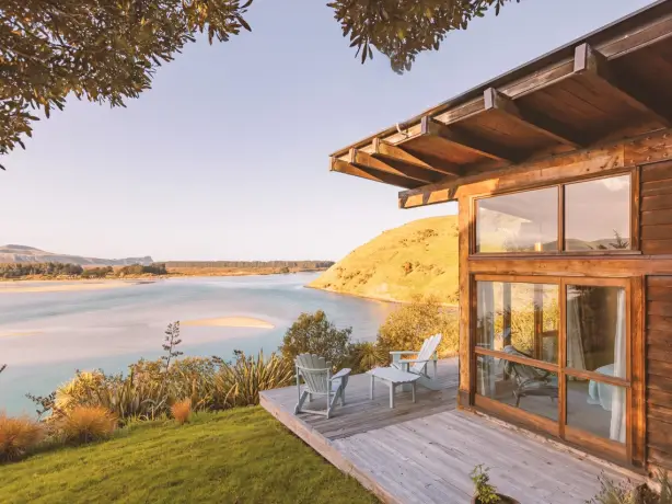 Stilvolles Holzhaus mit Terrasse und zwei Stühlen mit Blick über eine Bucht in Neuseeland
