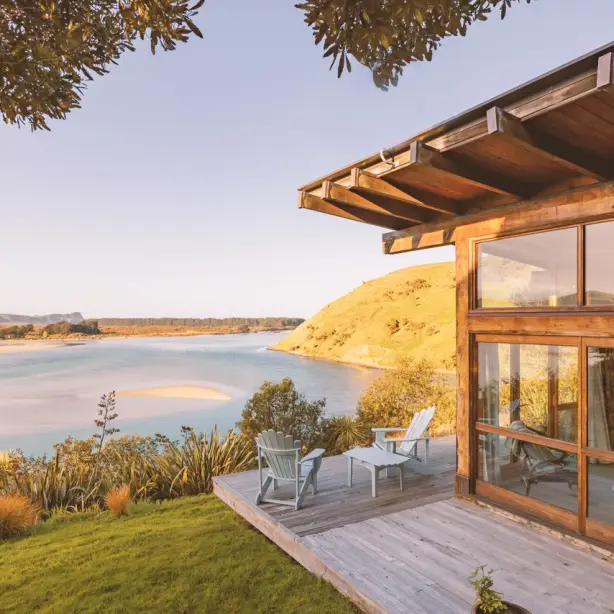 Stilvolles Holzhaus mit Terrasse und zwei Stühlen mit Blick über eine Bucht in Neuseeland