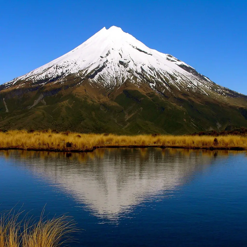 Ein schneebedeckter Berg im Hintergrund, der sich im See spiegelt, Mount Taranaki im Egmont National Park - Neuseeland