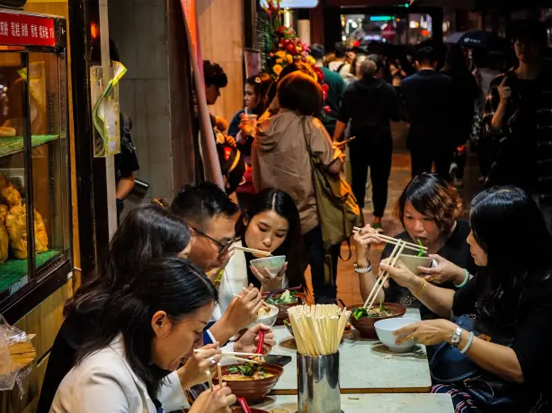 A family sitting at a table eating food outside a restaurant in Hong-Kong