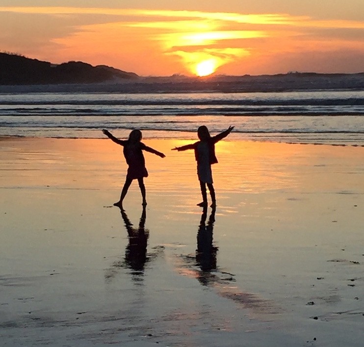 Zwei Kinder tanzen am Strand bei Sonnenuntergang in Neuseeland