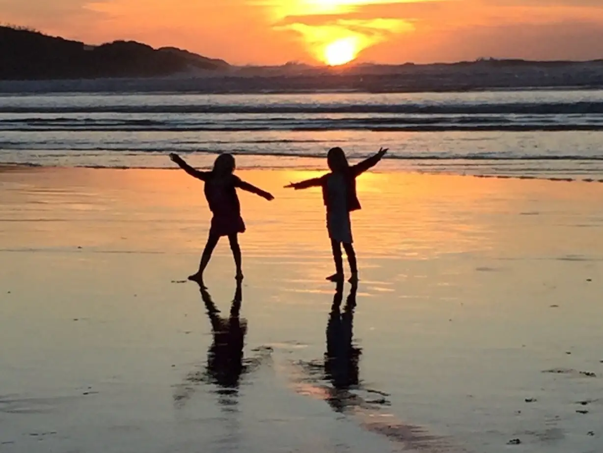 Two children dance on the beach at sunset in New Zealand