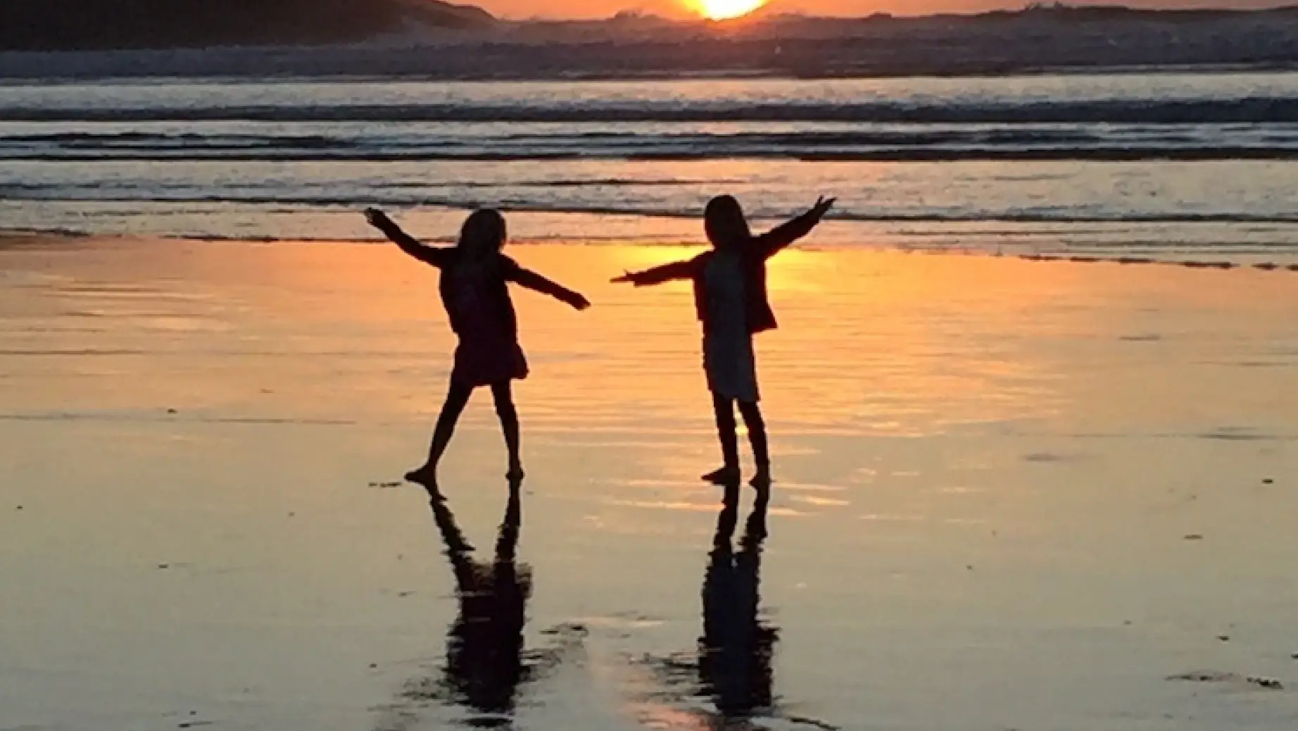 Zwei Kinder tanzen am Strand bei Sonnenuntergang in Neuseeland