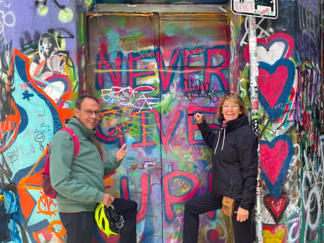 Paulien und Norbert posieren vor einer Graffiti-Wand mit der Aufschrift "Never Give Up".