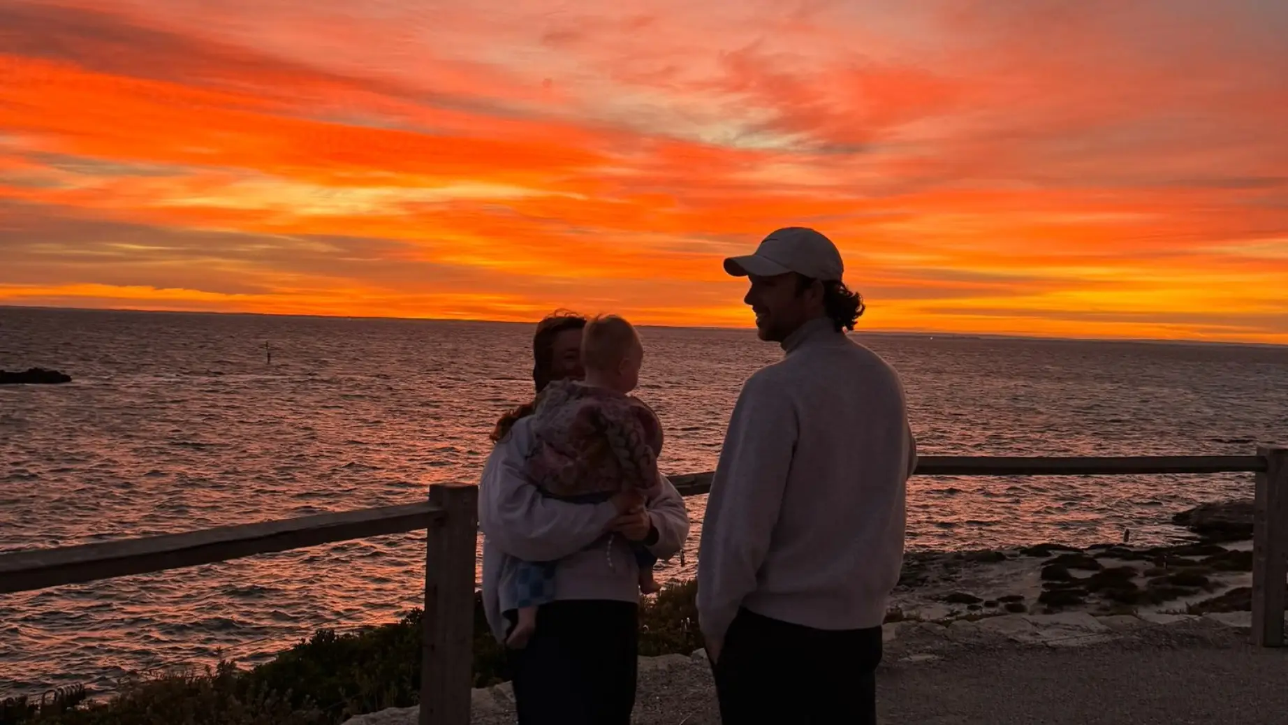 Junge Familie steht bei Sonnenuntergang am Meer