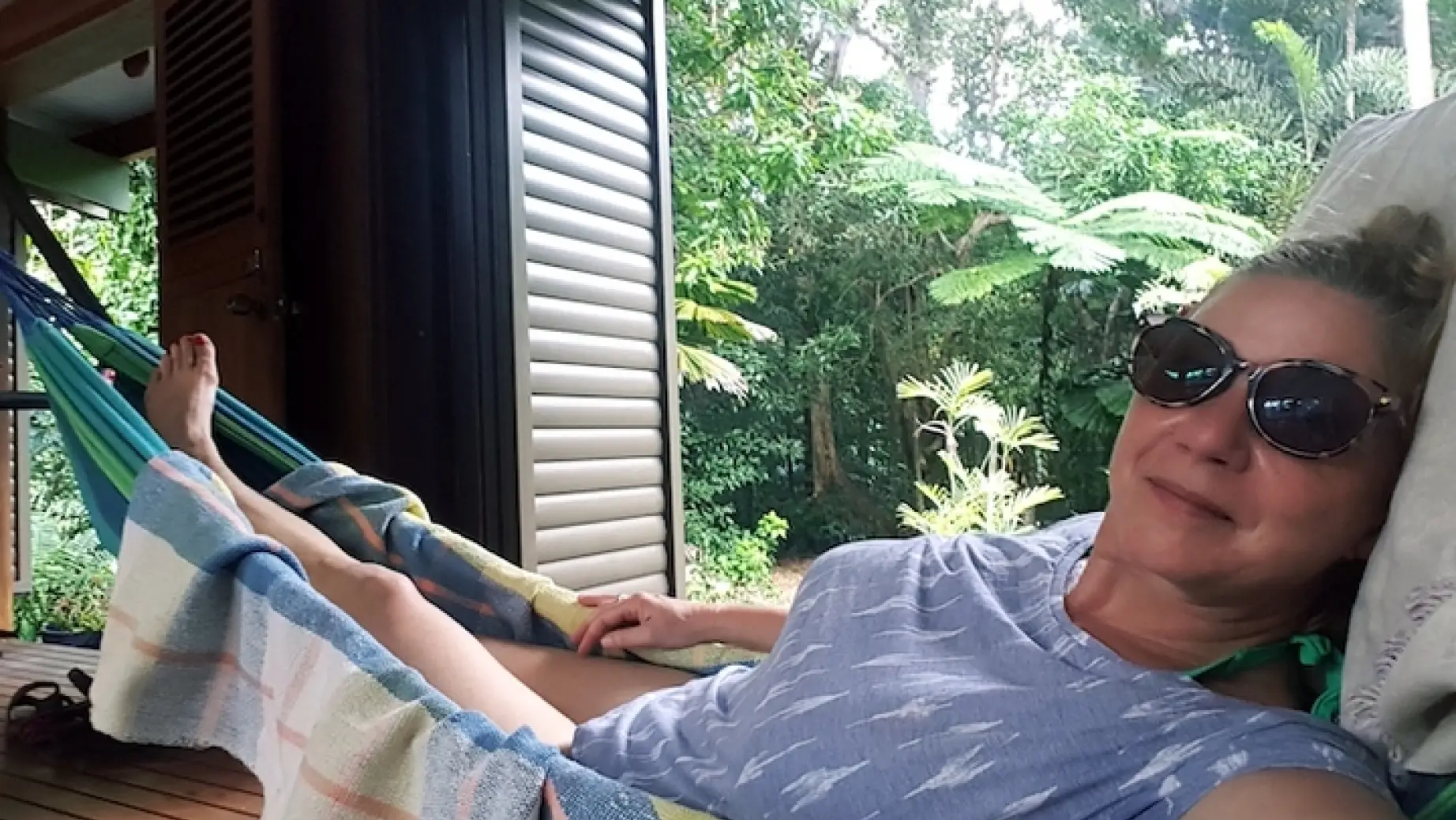 A lady relaxes in a hammock in a wooden cabin with rainforest in the background