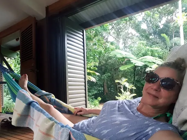 A lady relaxes in a hammock in a wooden cabin with rainforest in the background