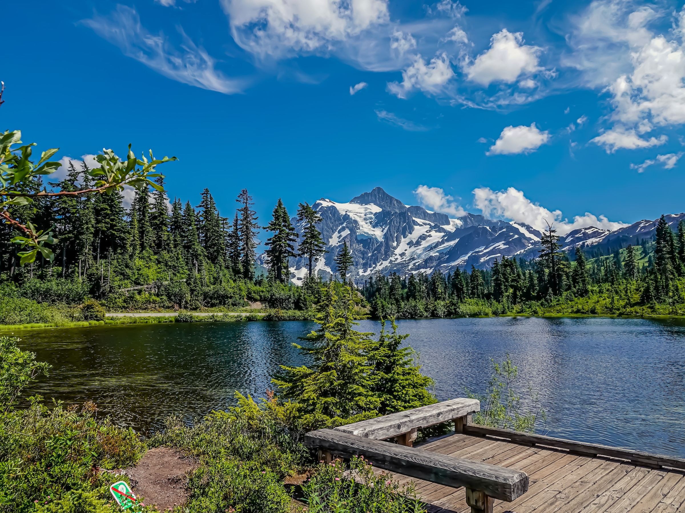 Ein friedlicher See im Mount Baker-Snoqualmie National Forest in Washington mit dichten Evergreens und schneebedeckten Gipfeln, die sich im Hintergrund erheben.