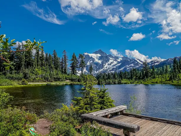 Ein friedlicher See im Mount Baker-Snoqualmie National Forest in Washington mit dichten Evergreens und schneebedeckten Gipfeln, die sich im Hintergrund erheben.