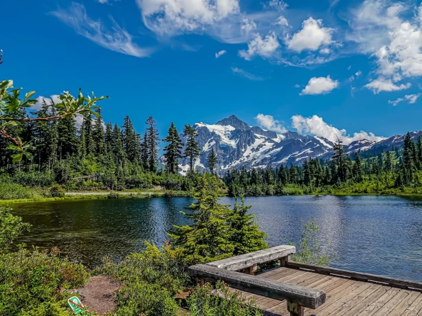 Ein friedlicher See im Mount Baker-Snoqualmie National Forest in Washington mit dichten Evergreens und schneebedeckten Gipfeln, die sich im Hintergrund erheben.