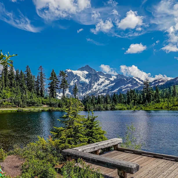 Ein friedlicher See im Mount Baker-Snoqualmie National Forest in Washington mit dichten Evergreens und schneebedeckten Gipfeln, die sich im Hintergrund erheben.