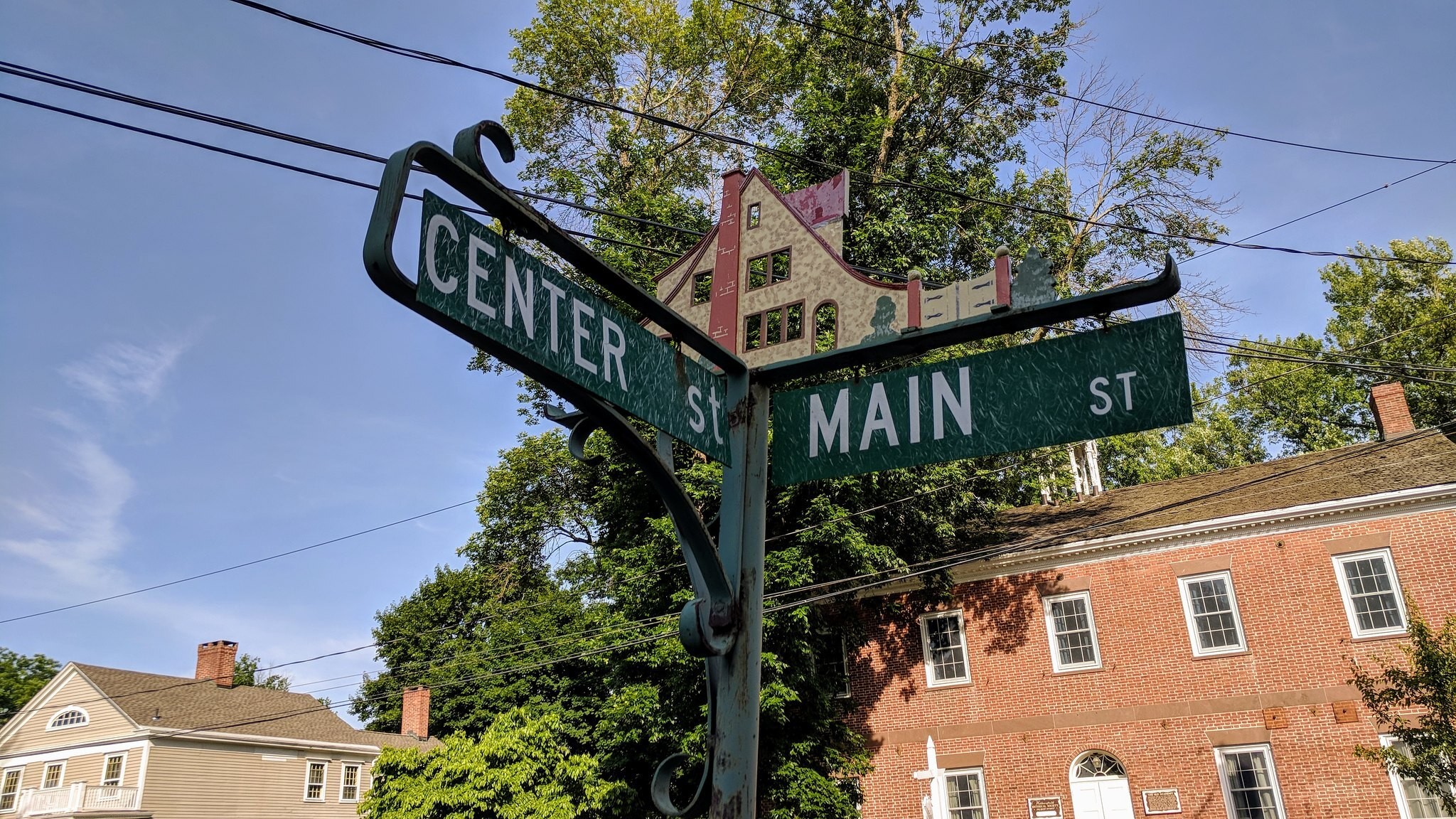 A vintage street sign marking the corner of Center Street and Main Street in a small American town, with historic brick buildings and trees in the background.
