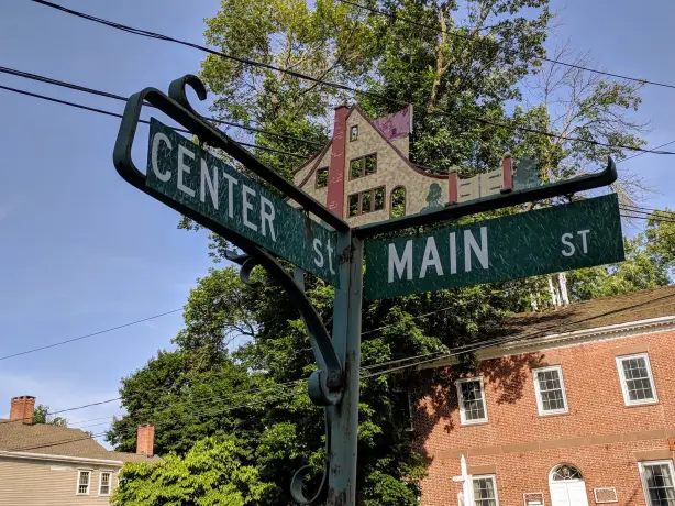 A vintage street sign marking the corner of Center Street and Main Street in a small American town, with historic brick buildings and trees in the background.