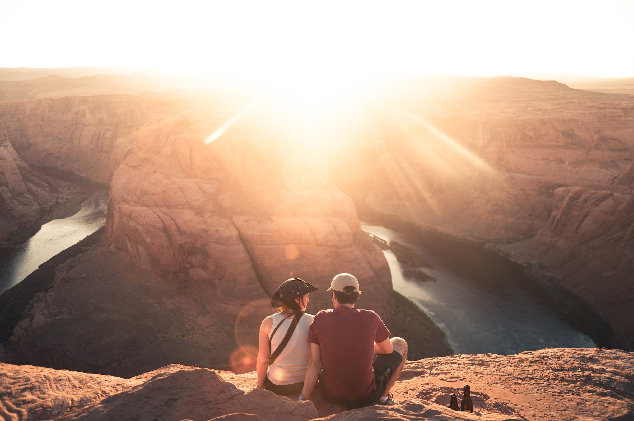 Ein Paar sitzt mit Blick auf Horseshoe Bend in Moab, Arizona, während die Sonne direkt in die Linse scheint.