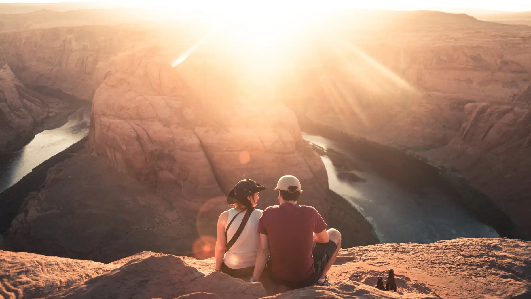 A couple sit overlooking Horseshoe Bend in Moab, Arizona with the glare of the sun hitting the lens