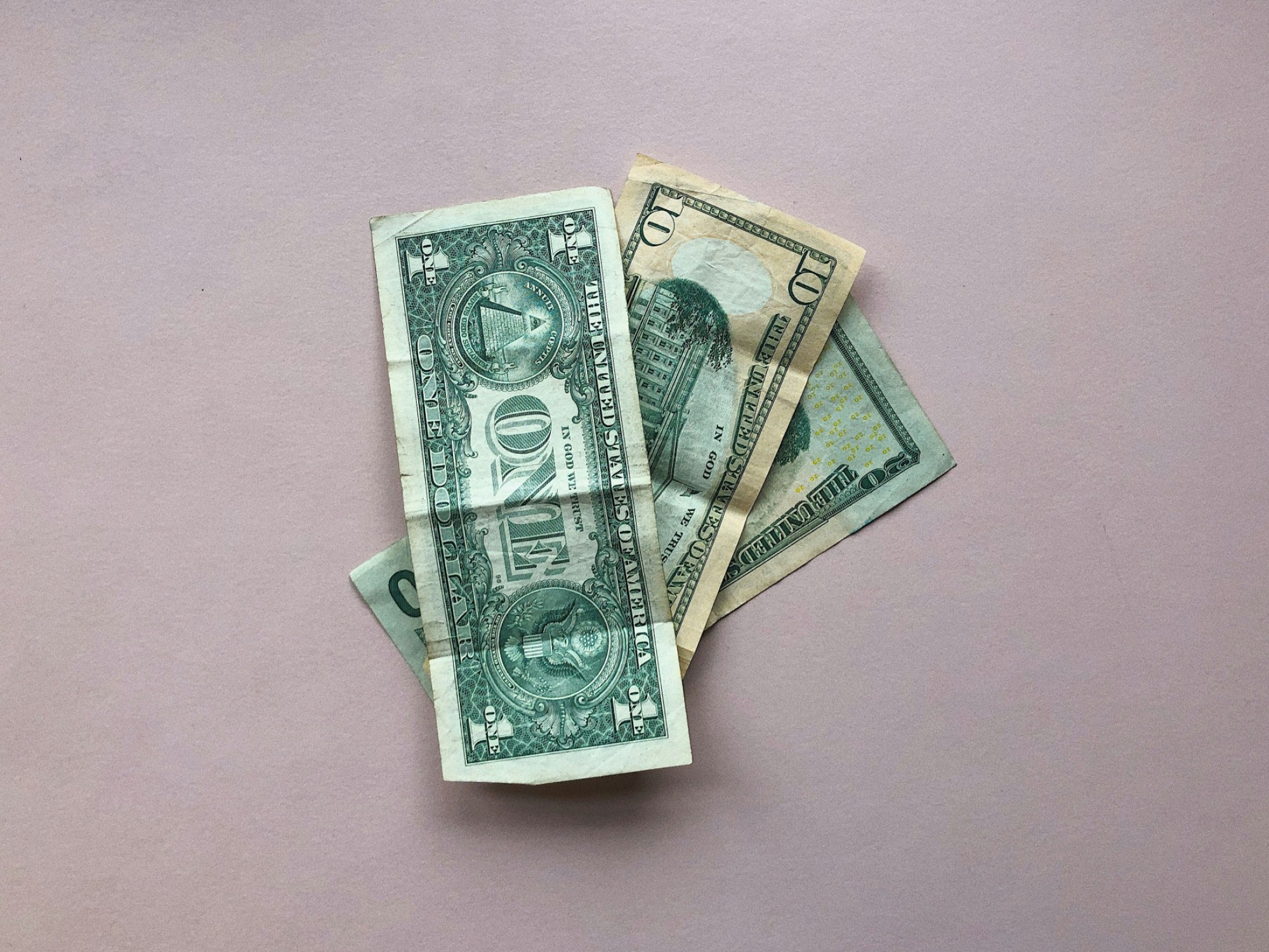 Ein kleiner Stapel von US-Dollarnoten liegt auf einer blassrosa Fläche.