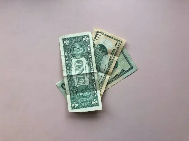 Ein kleiner Stapel von US-Dollarnoten liegt auf einer blassrosa Fläche.