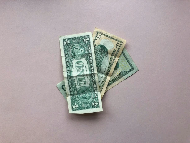 Ein kleiner Stapel von US-Dollarnoten liegt auf einer blassrosa Fläche.