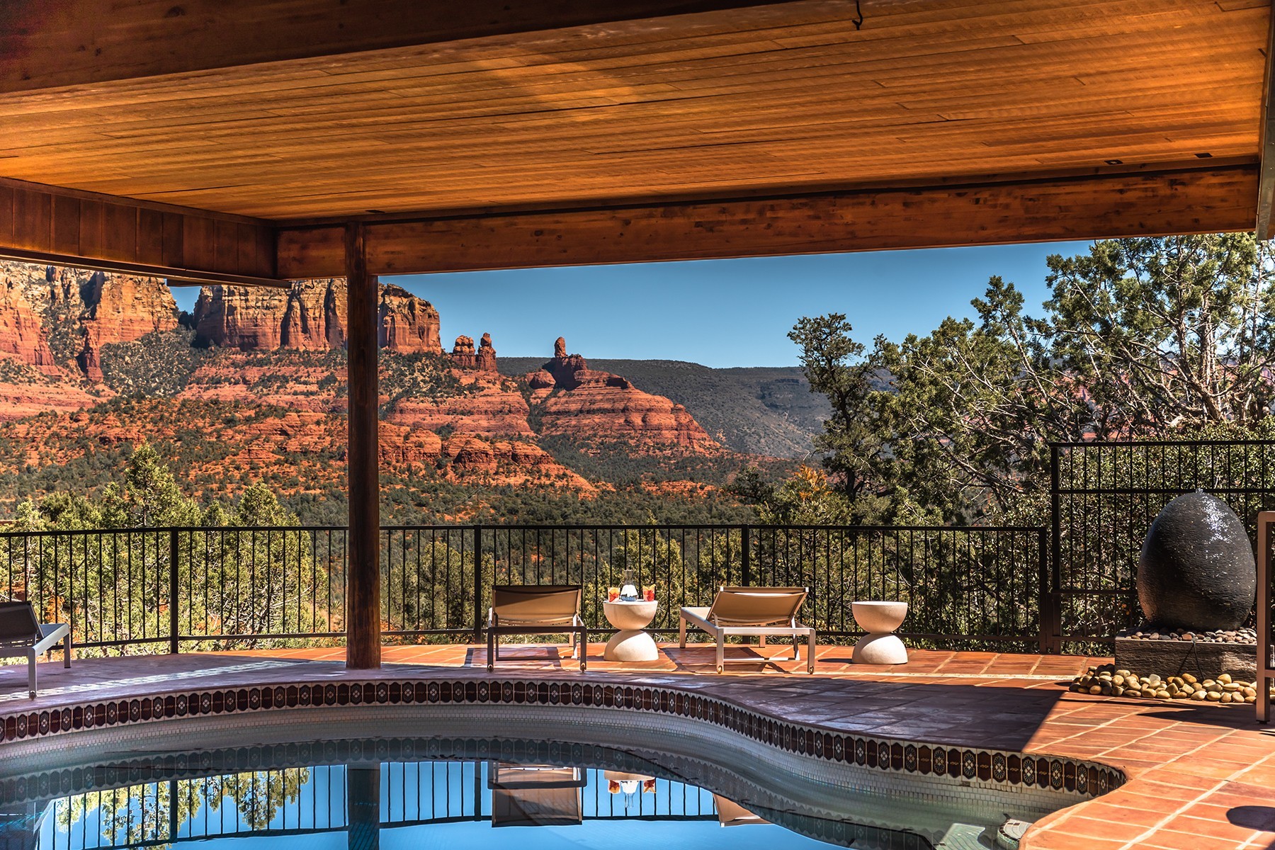Private Poolterrasse mit Sonnenliegen unter einem Holzdach, mit weitem Blick über die ikonischen roten Felsformationen von Sedona, Arizona USA unter einem klaren blauen Himmel