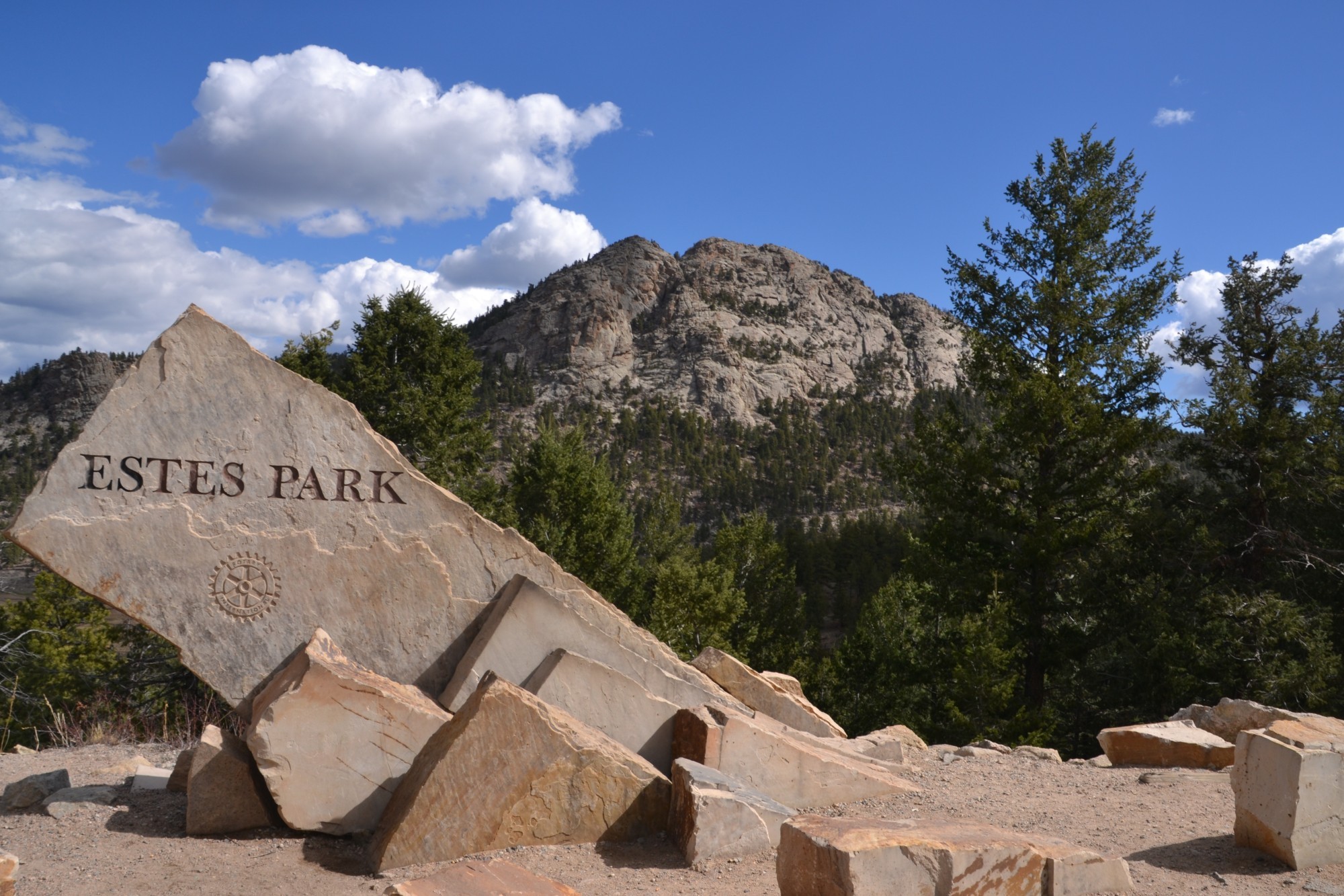 Eingangsschild von Estes Park steht vor einer Bergkulisse umgeben von Felsen und Nadelbäumen