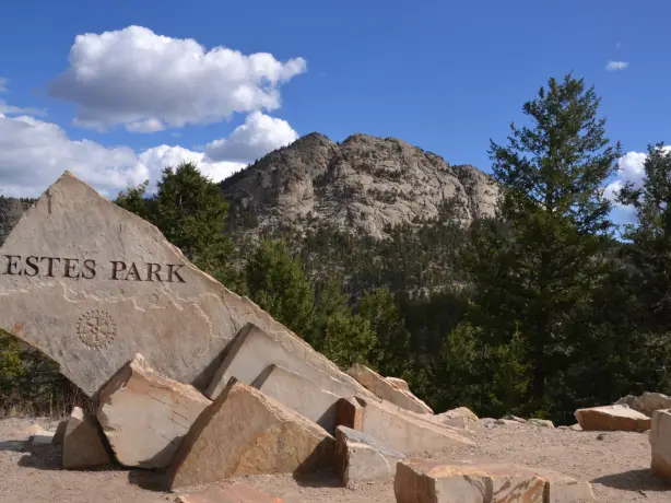 Eingangsschild von Estes Park steht vor einer Bergkulisse umgeben von Felsen und Nadelbäumen