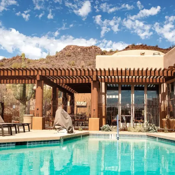 Südwestlich gestaltete Boutique-Hotel-Poolterrasse in Scottsdale, Arizona USA, mit Sonnenliegen und einer Holzpergola vor der Kulisse felsiger Wüstenhügel und Saguaro-Kakteen unter blauem Himmel