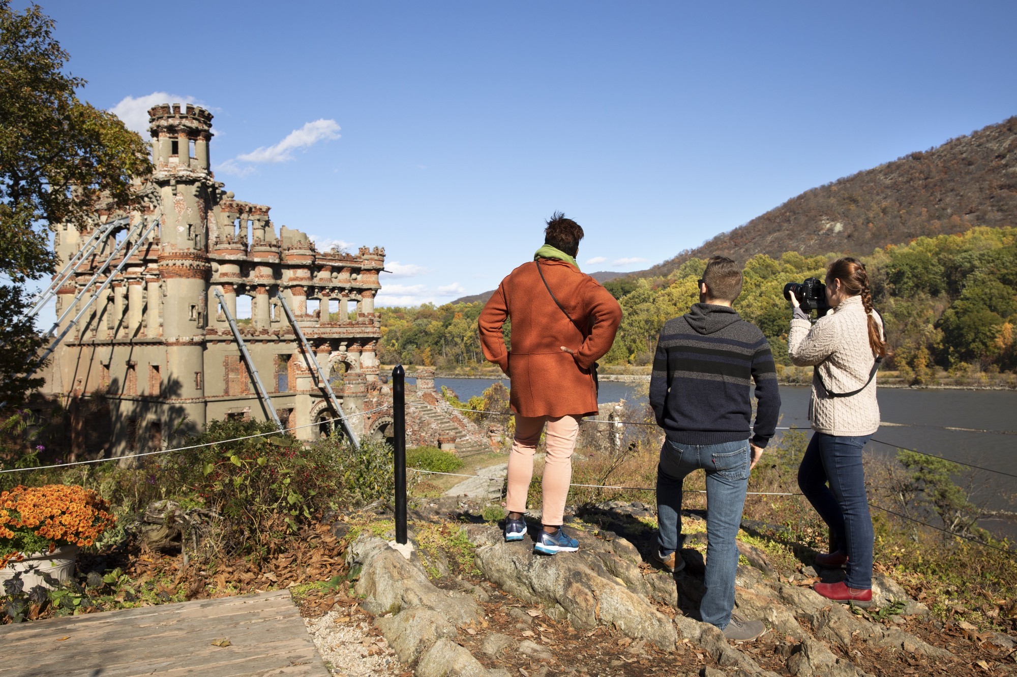 Drei Personen stehen hinter Absperrung und fotografieren eine Schloss-Ruine