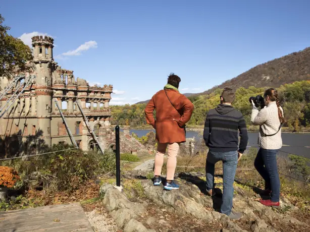Drei Personen stehen hinter Absperrung und fotografieren eine Schloss-Ruine