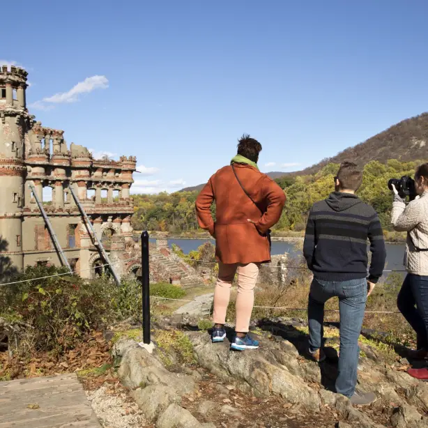 Drei Personen stehen hinter Absperrung und fotografieren eine Schloss-Ruine