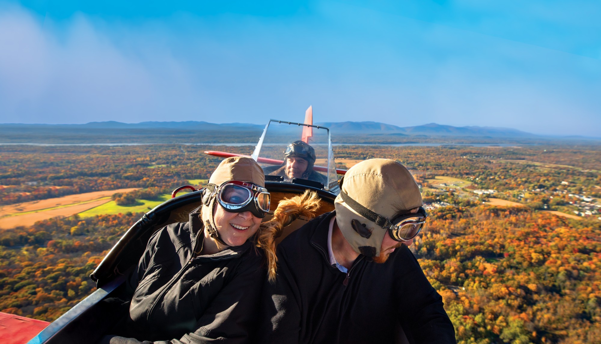 Drei Personen fliegen in historischem offenen Flugzeug über Herbstlandschaft in den USA
