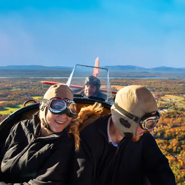 Drei Personen fliegen in historischem offenen Flugzeug über Herbstlandschaft in den USA