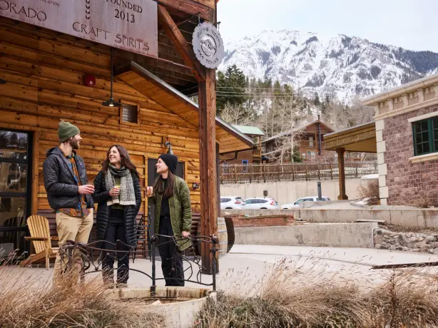 Drei Freunde genießen gemeinsam einen Drink vor einer Craft-Destillerie in Ouray, Colorado