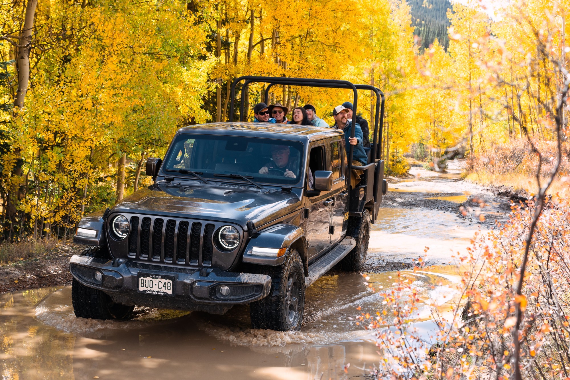 Ein Jeep mit Passagieren fährt durch eine teilweise geflutete Straße und einen herbstlichen Wald in Ouray, Colorado