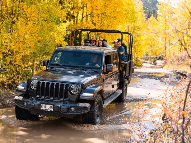 Ein Jeep mit Passagieren fährt durch eine teilweise geflutete Straße und einen herbstlichen Wald in Ouray, Colorado